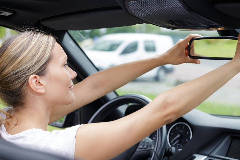 woman adjusting the rear view mirror in her car